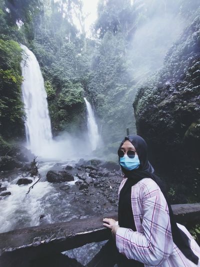 Portrait of woman wearing mask standing by waterfall in forest