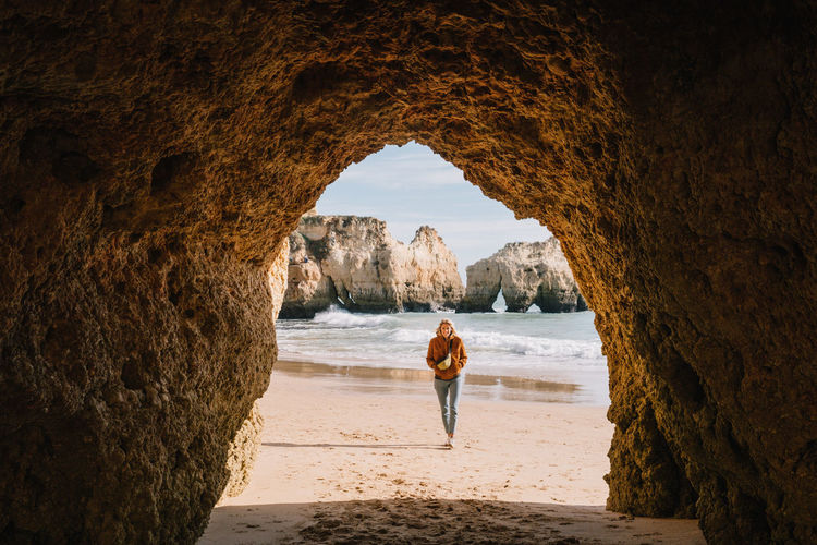 Woman walking at beach seen through cave