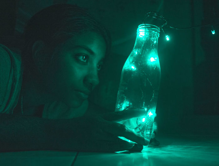 Woman looking at illuminated lights in bottle at home