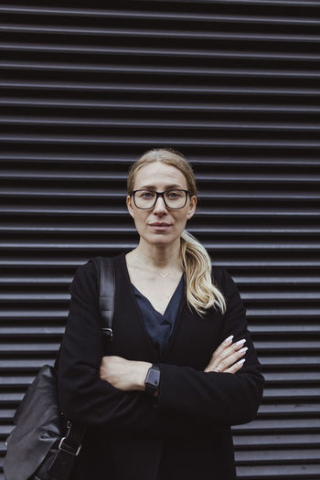 Portrait of businesswoman with arms crossed standing against shutter in city