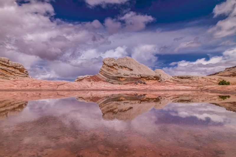 Pond by rock formations against cloudy sky