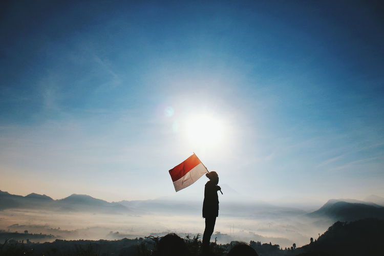 A young man carries an indonesian flag against the mountains at sunrise