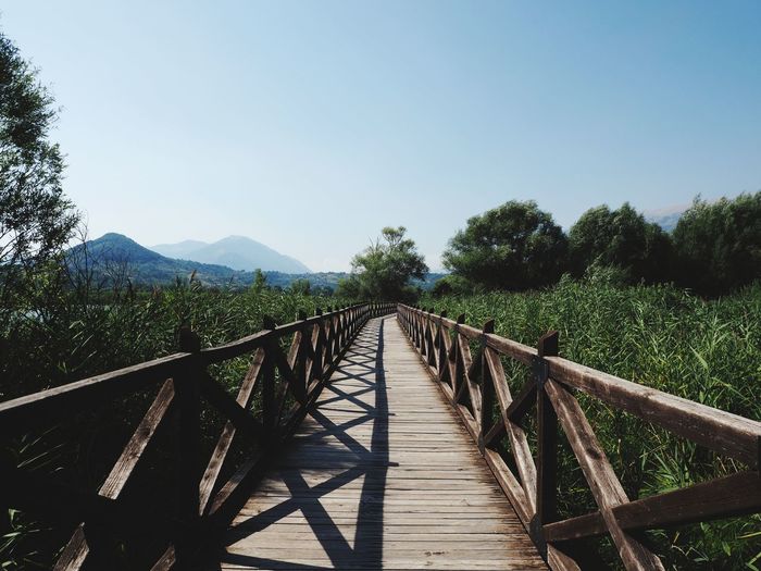 Wooden footbridge leading to mountains against clear sky