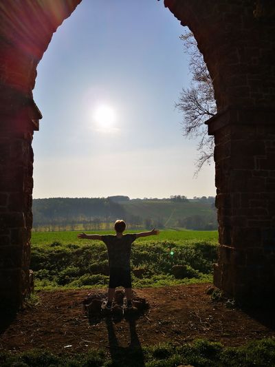 Rear view of boy with arms outstretched standing on land against sky