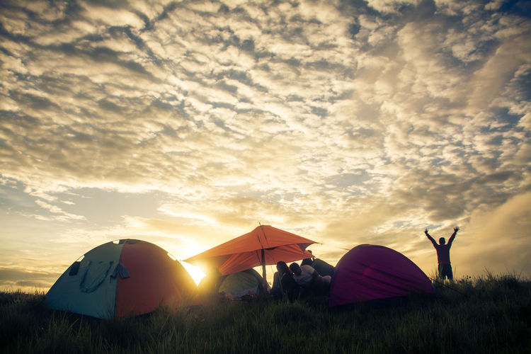 People camping on field against sky during sunset