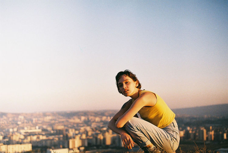 Portrait of young woman in city against clear sky