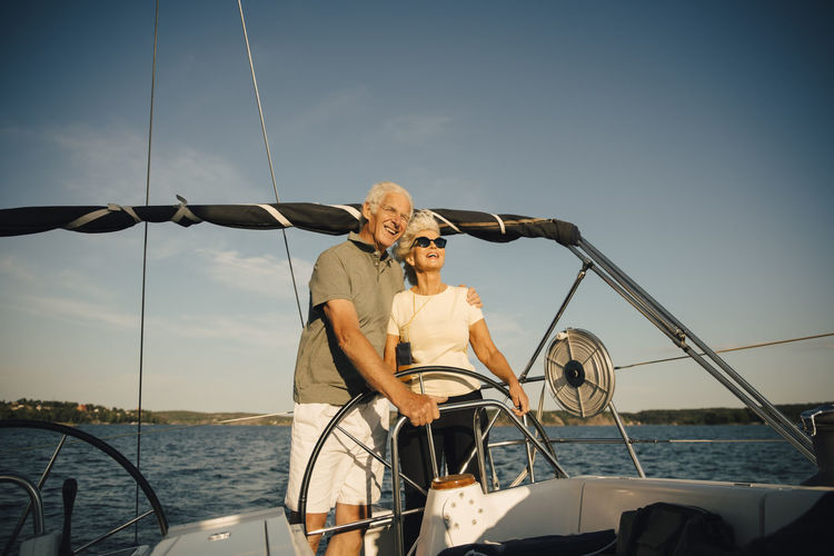Smiling senior couple with arm around in sailboat against sky in sea