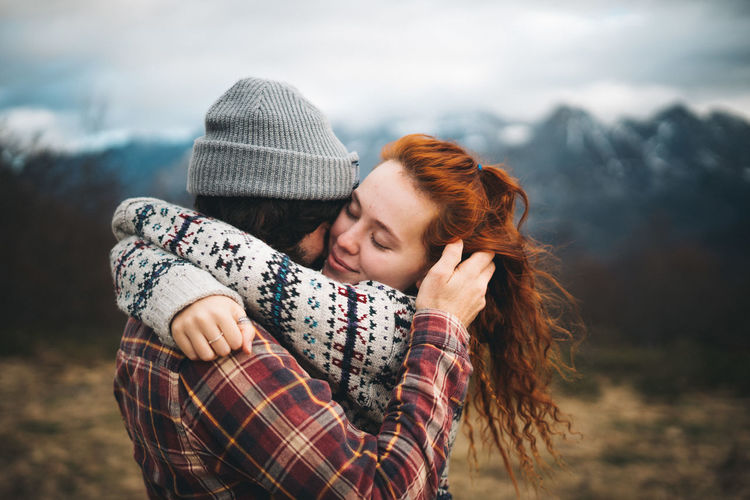 Side view of tender couple hugging and bonding with closed eyes in cold day in mountains