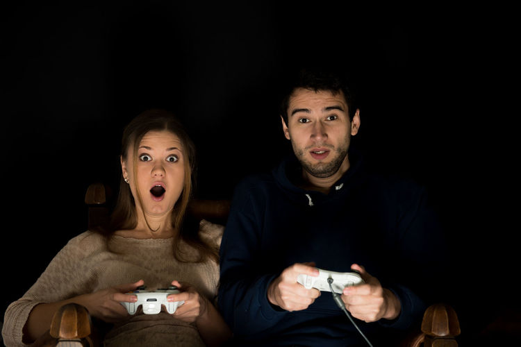 Portrait of couple playing video game against black background