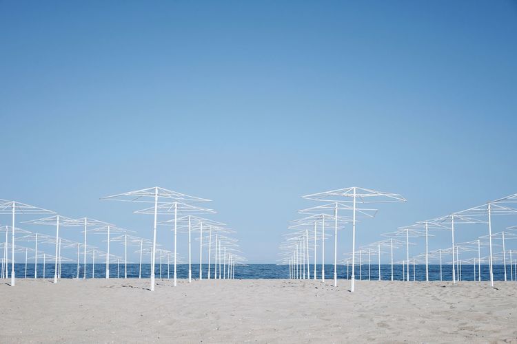 Empty parasols on beach against clear blue sky