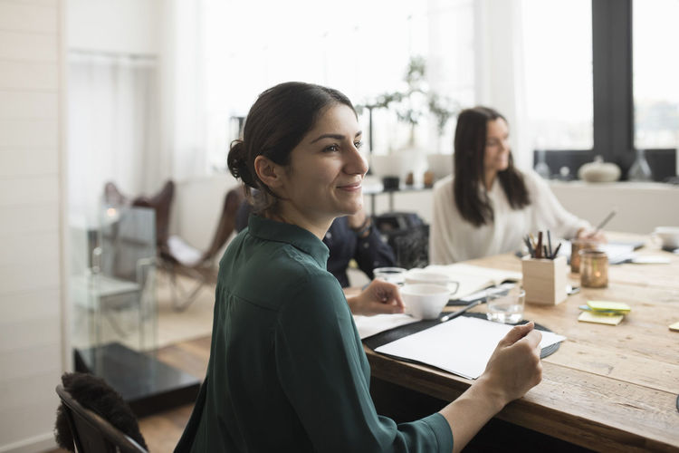 Smiling businesswoman sitting with colleagues at table in meeting