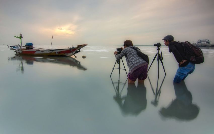 People photographing boats in sea against sky