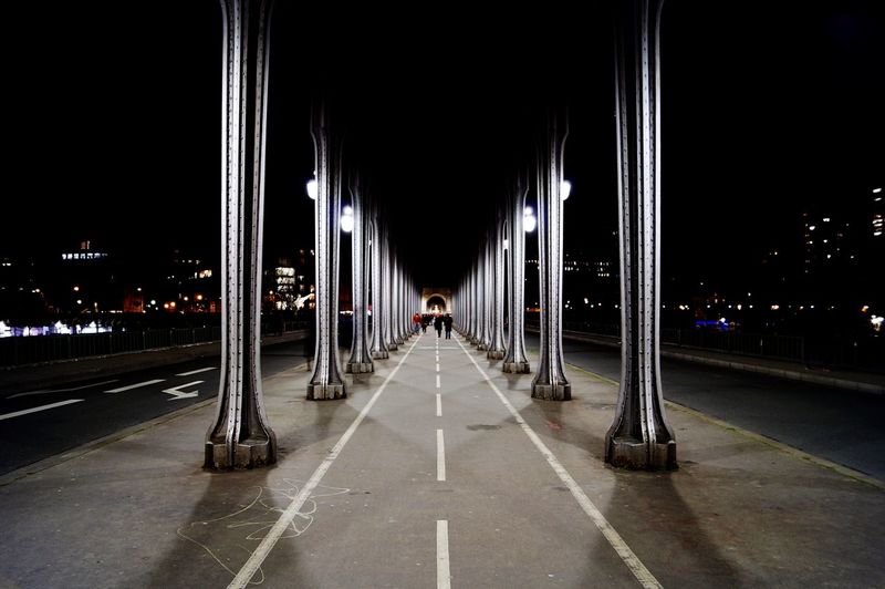 View of illuminated road under bridge in city at night