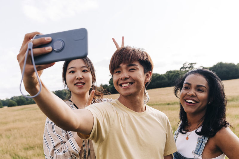 Smiling friends taking selfie through mobile phone at park