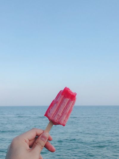 Hand holding ice cream over sea against clear sky