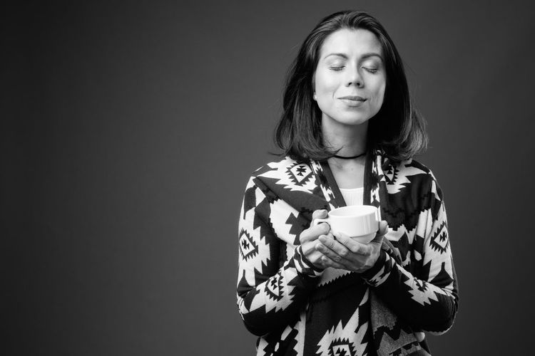 Mid adult woman holding coffee cup against black background