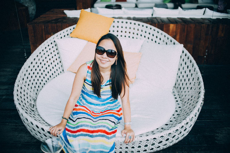 High angle portrait of smiling woman wearing sunglasses sitting on chair