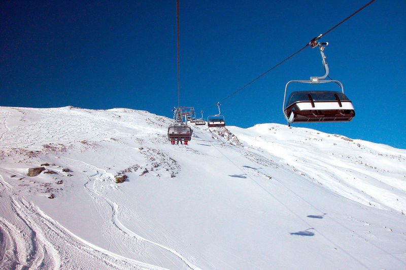 Chairlift in alpine ski area, clear blue sky, mountain slope covered in snow