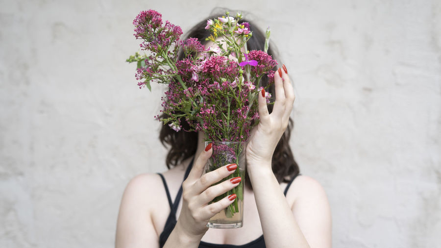 Midsection of woman holding bouquet against wall