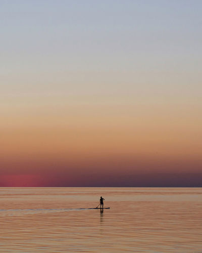 Silhouette person on the sup board on sea against sky during sunset. 