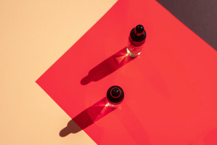 Two glass bottles with cosmetic liquid on bright red background with shadows and light reflections. 