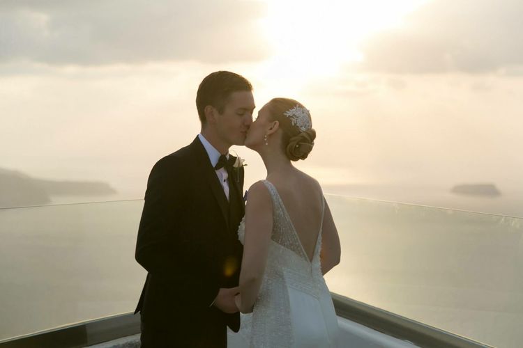 Bride and groom kissing at balcony against sea during sunset