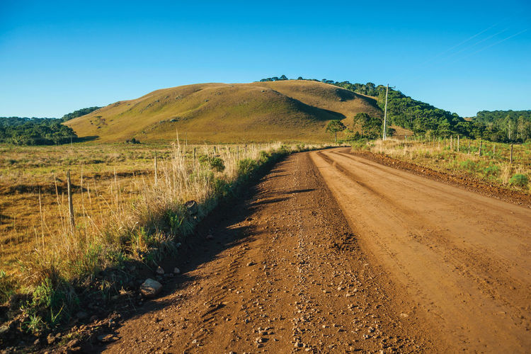 Deserted dirt road passing through rural lowlands with green hills near cambará do sul. brazil.