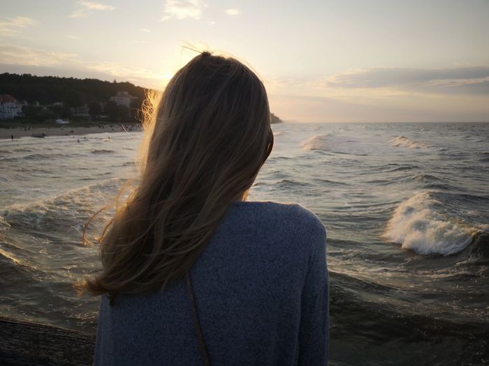 Rear view of woman standing by sea during sunset