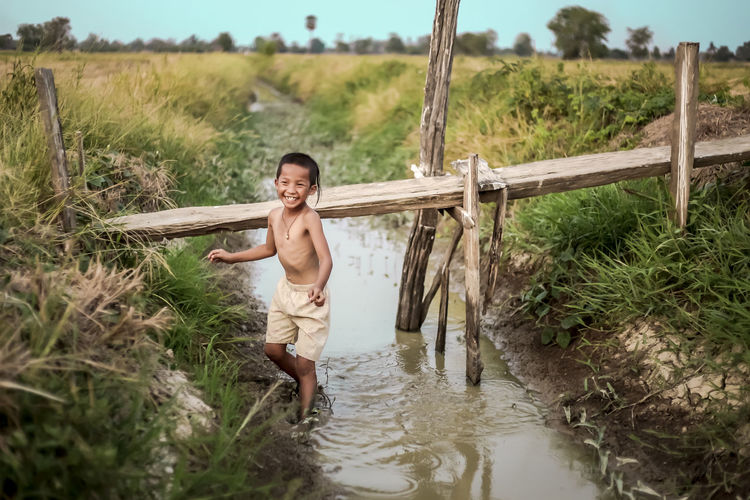 Smiling boy standing on canal at farm against sky