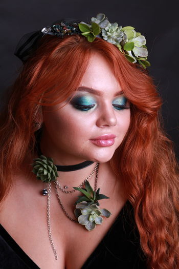 Sensuous young woman wearing wreath and necklace against black background