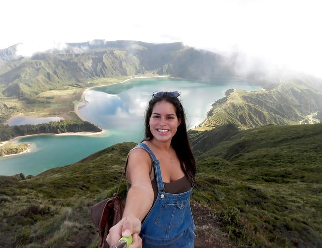 Portrait of smiling young woman standing at lake against sky