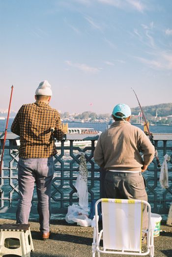 Rear view of male friends fishing by sea against sky