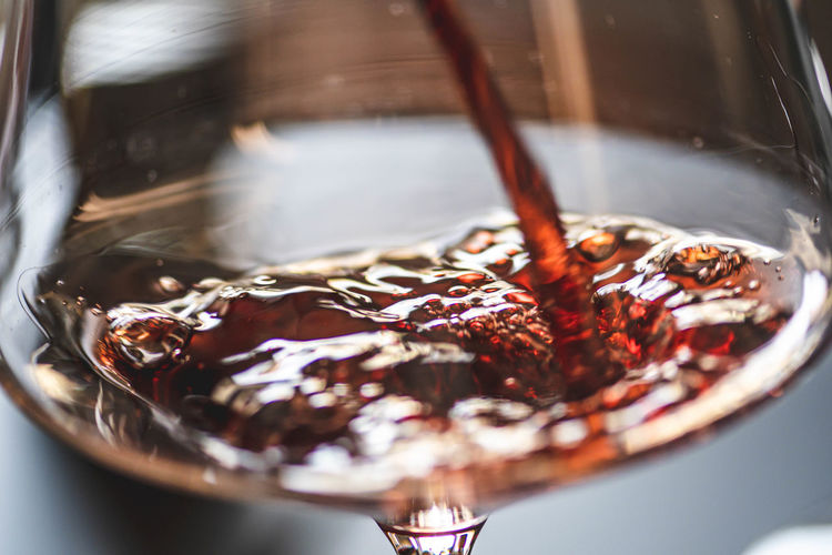 Pouring red wine into a wine glass with bubbles, close up