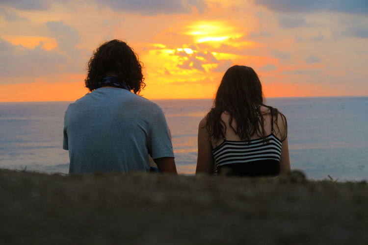 Rear view of couple sitting on beach at sunset