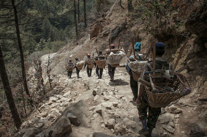 Rear view of people with baskets on mountain trail walking towards namche bazaar
