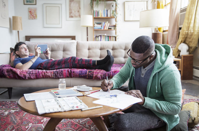 Homosexual man drawing while partner using tablet computer at home