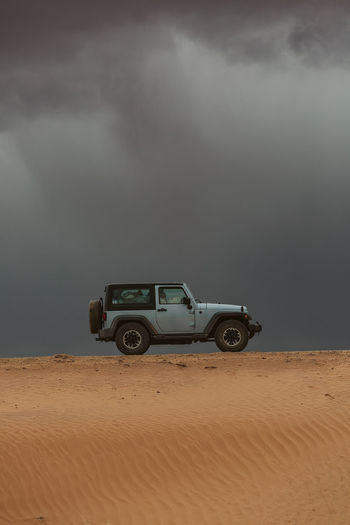Jeep drives across sand dune dirt road on road trip under storm clouds