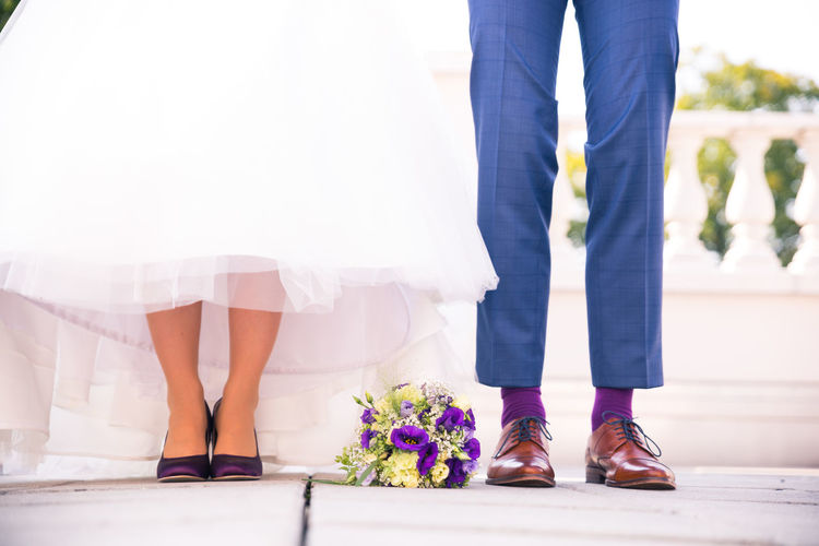 Low section of bride and groom with flower bouquet standing on floor