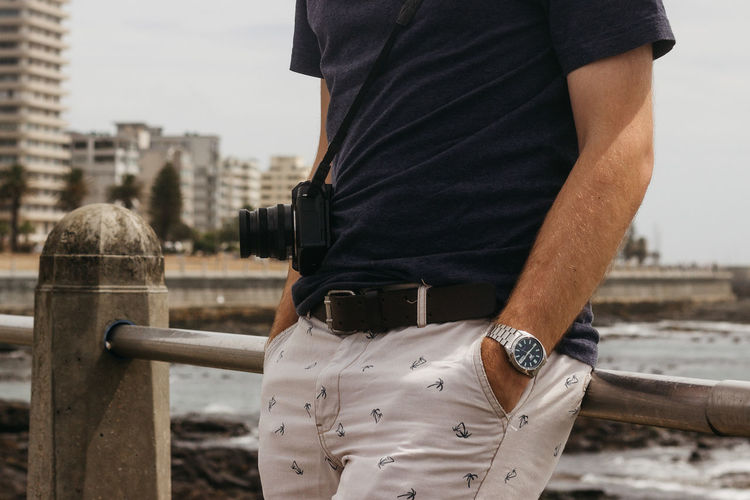 Midsection of man with hands in pockets leaning on railing