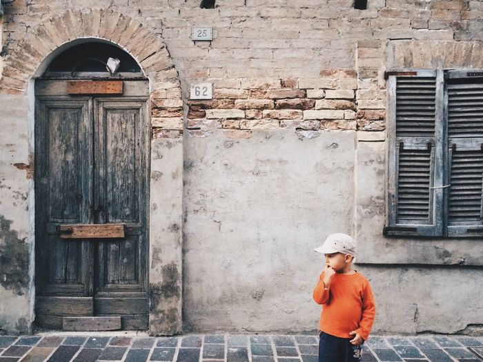 Confused little boy standing on sidewalk against historic building