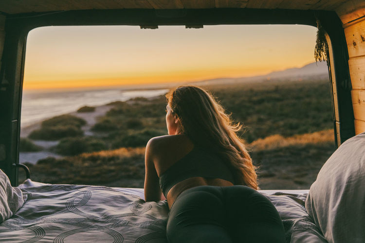 Young woman looking out to ocean from bed of sprinter van in mexico.