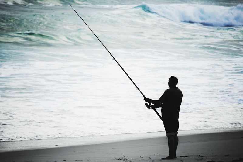 Silhouette man fishing on beach