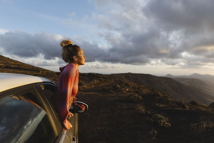 Young woman leaning out of car window looking at mountain landscape