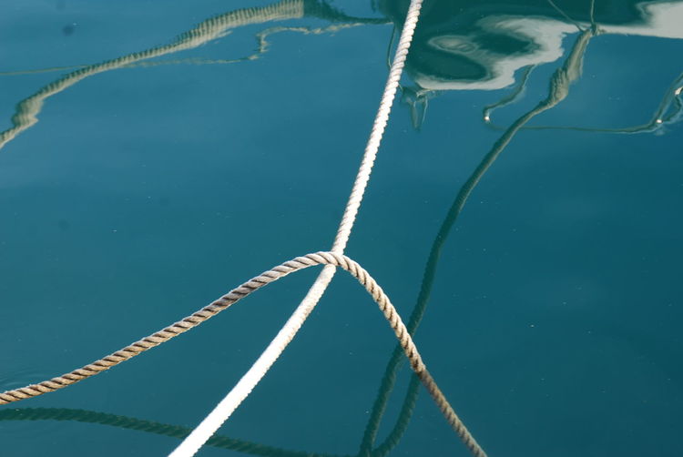 Ropes that tide the boats to the pier, with reflection on the bright sunny summer day.