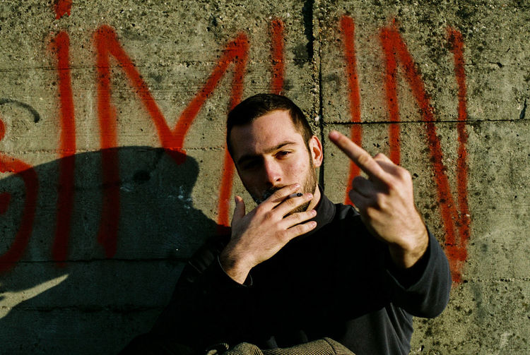 Portrait of young man smoking cigarette against wall