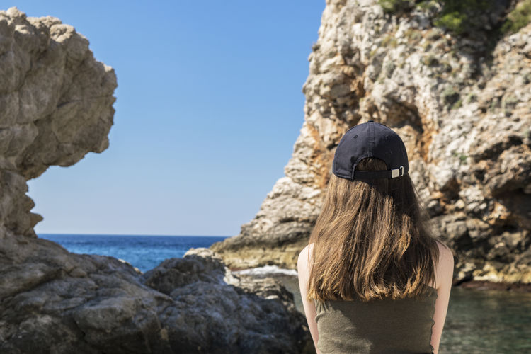 Rear view of woman with long hair wearing cap while looking at sea against sky