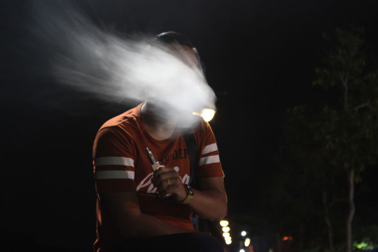 Man emitting smoke while holding cigarette outdoors