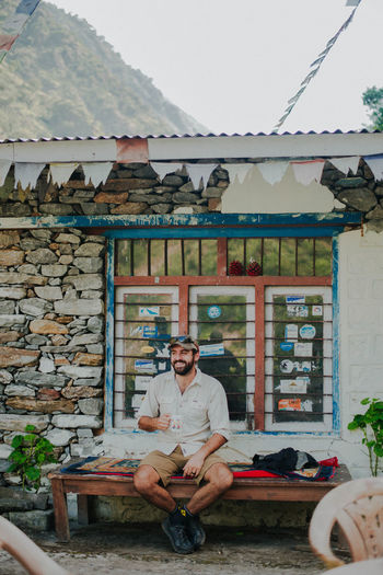 Smiling male hiker resting on bench with beverage in hand in mountains