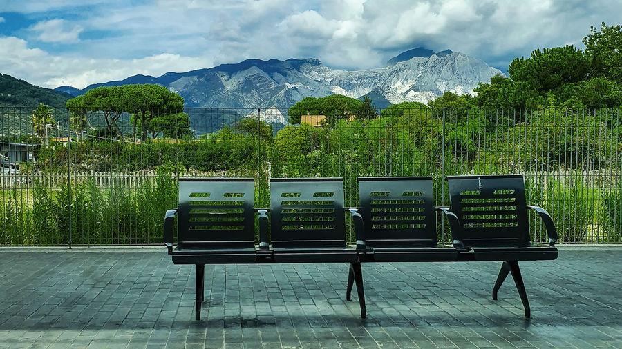 Empty bench against trees and mountains against sky
