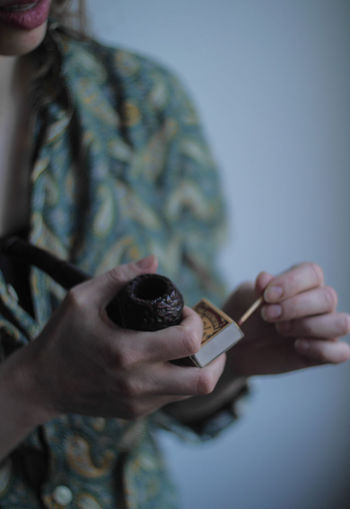 Midsection of mid adult woman holding matchstick and pipe while standing against wall